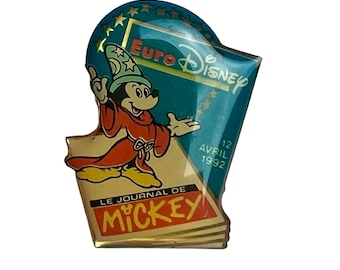 May include: A gold-colored pin featuring Mickey Mouse dressed as a wizard, holding a magic wand. The pin is shaped like a folded newspaper with the text "Le Journal de Mickey" and "Euro Disney" on it. The date "12 Avril 1992" is also visible.