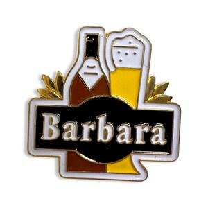 Pode incluir: Pin de metal dourado com uma garrafa marrom e um copo de cerveja amarelo. O pin tem um fundo branco com uma faixa preta que diz "Barbara".