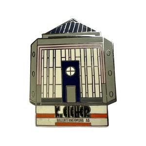 May include: A silver metal pin shaped like a building with a blue window and the text "K. EICHER BAUNTERNEHMUNG AG" on the bottom.