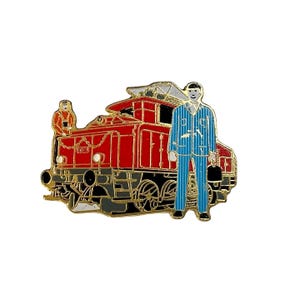 May include: A red and gold train pin featuring a conductor and a passenger. The train is a detailed illustration with the number "1073" visible. The conductor is wearing a blue striped uniform and holding a black bag.