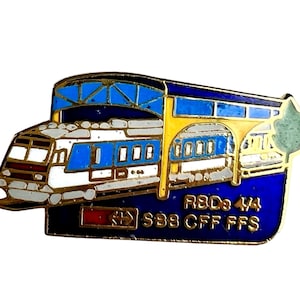 May include: A blue and yellow enamel pin featuring a train under a blue and yellow canopy. The pin has the text "RBD 3 1/4 SBB CFF FFS" on the bottom.