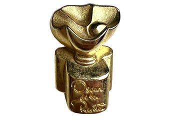 May include: Gold-toned metal brooch with a flower-shaped design and the inscription "Oscar de la Renta" on the base.