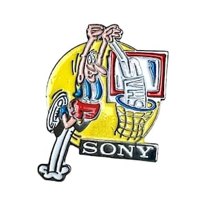 Könnte beinhalten: Ein farbenfroher Emaille-Pin mit einer Cartoonfigur, die einen VHS-Tape in einen Basketballkorb wirft. Der Pin hat einen gelben Hintergrund und das Wort "SONY" unten.