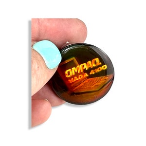 May include: A round, dark brown, glass paperweight with a gold-colored image of a Compaq laptop and the text "Compaq Mada 4100".