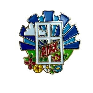 May include: A gold-coloured pin featuring a white window frame and a blue and green sunburst design. The word "AJAX" is written in red letters inside the window. There are colourful flowers at the bottom of the pin.