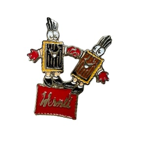 May include: A gold-colored pin with two cartoon characters standing on a red box with the word "Werther's" printed on it. The characters are wearing brown and black outfits and have red gloves.