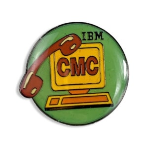Könnte beinhalten: Ein runder, grüner IBM CMC-Anstecker mit einem braunen Telefonhörer und einem gelben Computerbildschirm. Der Anstecker trägt oben den Text "IBM" und "CMC" auf dem Bildschirm. Ein Vintage-Artikel.