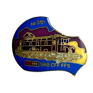 May include: A metal enamel pin featuring a brown locomotive train with the text Ae 3/61 and SBB CFF FFS. The design includes a blue background with purple and yellow accents, outlined in gold metal, depicting a classic Swiss railway engine.