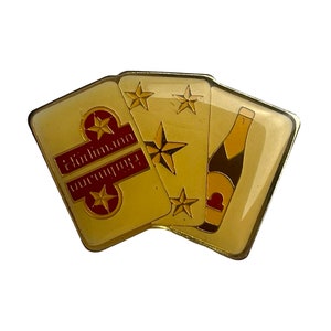 Pode incluir: Pin dourado com três cartas de jogar, uma com uma garrafa de champanhe e duas com estrelas. As cartas mostram o texto "Congratulations" em vermelho.