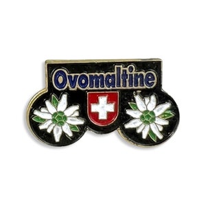 May include: A gold-coloured pin with a black background featuring the text "Ovomaltine" in blue letters. The pin also has a red shield with a white Swiss cross and two white edelweiss flowers with green centres.