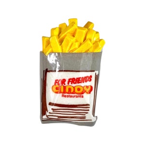 May include: A yellow and brown paper bag with a white label that says "For Friends Cindy Restaurants". The bag is filled with yellow chips.