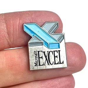 Pode incluir: Um broche de metal com o logótipo do Microsoft Excel. O design inclui uma forma de X estilizada em azul e cinzento posicionada sobre uma base retangular prateada. O texto Microsoft EXCEL está impresso a preto na base prateada.