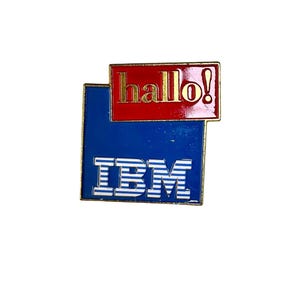 May include: A blue and red enamel pin with the text "hallo!" in red and "IBM" in white with blue stripes.