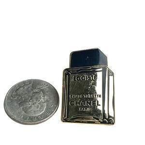 Puede incluir: Pin de metal dorado con forma de frasco de perfume. El frasco es negro y tiene las palabras "Egoiste" y "Eau de Toilette Chanel Paris" en &eacute;l.