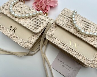 May include: Two small straw purses with pearl straps. The purses are beige and have a cream colored flap with gold lettering. The purses are labeled "AR" and "AN".