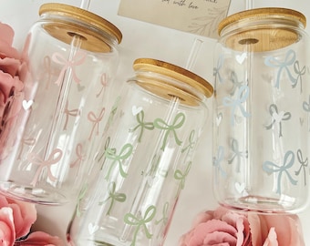 May include: Three clear glass tumblers with bamboo lids and straws. The tumblers are decorated with bows and hearts in pink, green, and blue. A card reads "CUSTOM GIFTS BY ELLE Created with love."