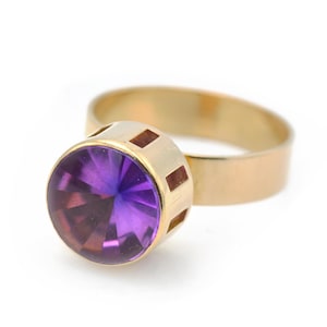 May include: A gold ring with a large, round, purple amethyst gemstone. The ring has a simple band with a decorative cut-out design.