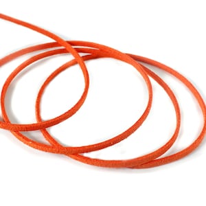 May include: Close-up of a vibrant orange leather cord, coiled into three loops, with a single strand extending upwards. The cord is set against a clean white background, highlighting its color and texture. Ideal for jewelry making or crafting.