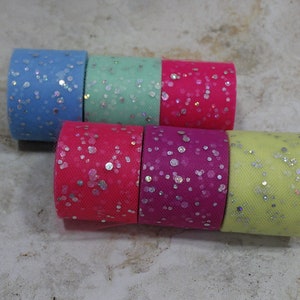 May include: Six rolls of colorful tulle fabric, each with a different color and silver glitter. The colors include light blue, mint green, hot pink, fuchsia, and yellow. The tulle is tightly rolled.