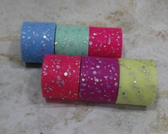 May include: Six rolls of colorful tulle fabric, each with a different color and silver glitter. The colors include light blue, mint green, hot pink, fuchsia, and yellow. The tulle is tightly rolled.