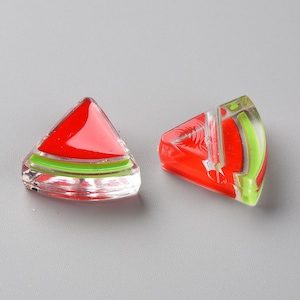 Puede incluir: Dos cuentas de vidrio con forma de sandía con detalles rojos, verdes y blancos. Las cuentas son transparentes y tienen un acabado brillante.