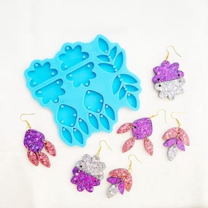 May include: A light blue silicone mold for making earrings, alongside several pairs of finished earrings. The earrings feature glitter in purple, silver, and pink, with gold-colored hooks. The mold has various floral and leaf shapes.