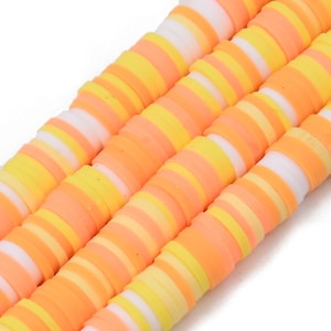 Puede incluir: Una hebra de cuentas de arcilla polimérica de colores. Las cuentas están rayadas de blanco, amarillo y naranja.