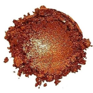 Puede incluir: Primer plano de un montón de polvo de mica de cobre. El polvo es de color naranja intenso con un brillo metálico.