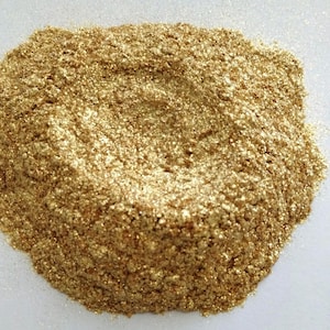 Pode incluir: Um close-up de um monte de glitter dourado fino. O glitter é de cor dourada metálica e tem uma textura fina e brilhante.