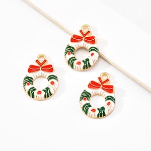 May include: Three gold-coloured Christmas wreath charms. Each charm features a white base with green and red accents, a red bow, and a loop for hanging. Ideal for festive jewellery or craft projects.