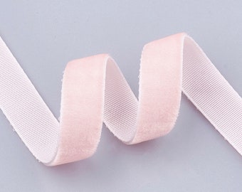 May include: A length of pale pink velvet ribbon, curled in a gentle wave. The ribbon has a soft, plush texture and a delicate, light color. The ribbon is set against a light gray background.