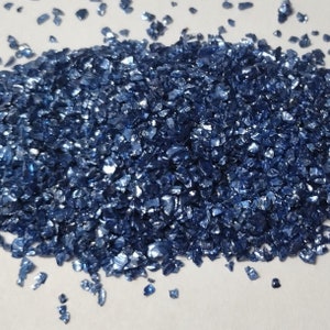 May include: A pile of blue iridescent glass glitter. The glitter is made of small, irregular pieces of glass that have a metallic sheen.