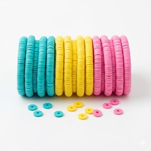 May include: Stacks of colorful clay disc beads in turquoise, yellow, and pink. Several loose beads of each color are scattered in front of the stacks. These beads are ideal for jewelry making and crafting projects.
