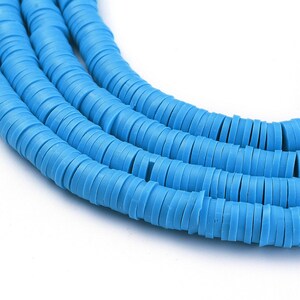 May include: A close-up of a strand of light blue round polymer clay beads. The beads are stacked on top of each other, creating a layered effect.