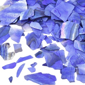 Könnte beinhalten: Ein Haufen irisierender blauer Glassplitter, verstreut auf einem weißen Hintergrund. Die Splitter sind in verschiedenen Größen und Formen, wobei einige einen stärker ausgeprägten irisierenden Effekt haben als andere.
