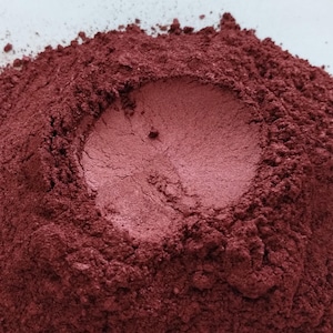Puede incluir: Un montón de polvo de mica rojo oscuro con una pequeña hendidura en el centro.