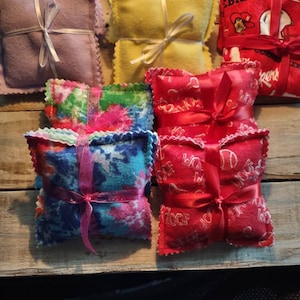 May include: Assortment of handmade fabric sachets in various colors and patterns, including purple, yellow, red, blue, and green. The sachets are tied with ribbon and have a decorative scalloped edge.