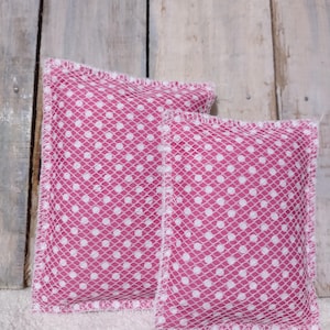 May include: Two pink and white polka dot fabric sachets. The sachets are rectangular and have a white mesh overlay. The edges are finished with a white stitched trim. The sachets are displayed on a white surface.