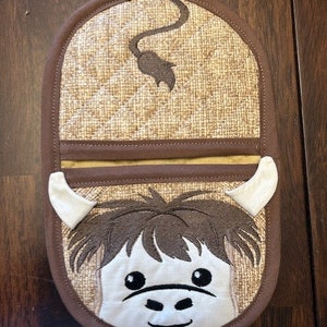 May include: Brown and tan oven mitt with a whimsical monkey face design. The mitt features a quilted pattern, a brown border, and a loop for hanging. The monkey face includes white horns, brown hair, and a smiling mouth.