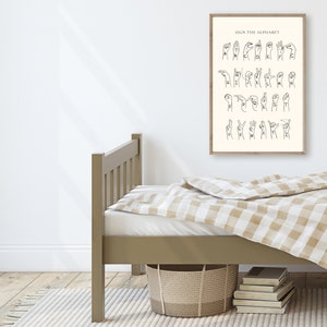 May include: A black and white illustration of the American Sign Language alphabet on a beige background. The illustration is framed and hanging on a white wall above a brown wooden bed with a beige and white checkered bedspread.