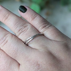 May include: A silver ring with a hammered texture. The ring features a double-band design that crosses over each other. The ring is worn on a finger.
