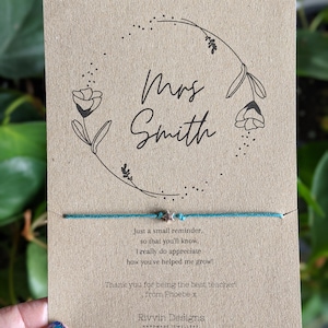 May include: A brown card with a floral design and the text "Mrs Smith" in black. A turquoise string bracelet with silver star charms is attached to the card. The card also includes the text "Just a small reminder, so that you'll know. I really do appreciate how you've helped me grow! Thank you for being the best teacher! from Phoebe x Rivvin Designs HANDMADE JEWELLERY".