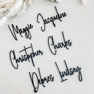 K&ouml;nnte beinhalten: Schwarze Acryl-Namensschilder mit den Namen Maggie, Jacqueline, Christopher, Charles, Debores und Lindsey in Kursivschrift.
