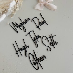 K&ouml;nnte beinhalten: Schwarze Acryl-Namen f&uuml;r eine Hochzeit oder ein Event. Die Namen sind Meghan, Paul, Hugh, Tyler, Colleen und Seth.