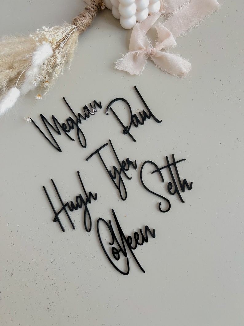 K&ouml;nnte beinhalten: Schwarze Acryl-Namen f&uuml;r eine Hochzeit oder ein Event. Die Namen sind Meghan, Paul, Hugh, Tyler, Colleen und Seth.