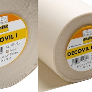 May include: Two rolls of beige fabric, one labelled "DECOVIL I" and the other "DECOVIL I LIGHT" by Vlieseline. Each roll is 90 cm wide and 15 m long. The fabric is 42% PES, 35% CV, and 23% PA. The labels include a beige colour swatch.