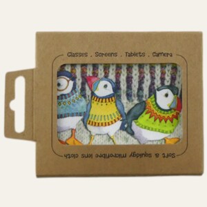 May include: A brown cardboard package with a window displaying three colorful puffin illustrations on a microfiber lens cloth. The puffins wear sweaters in blue, yellow, and green. Text on the package reads: "Glasses. Screens. Tablets. Camera."