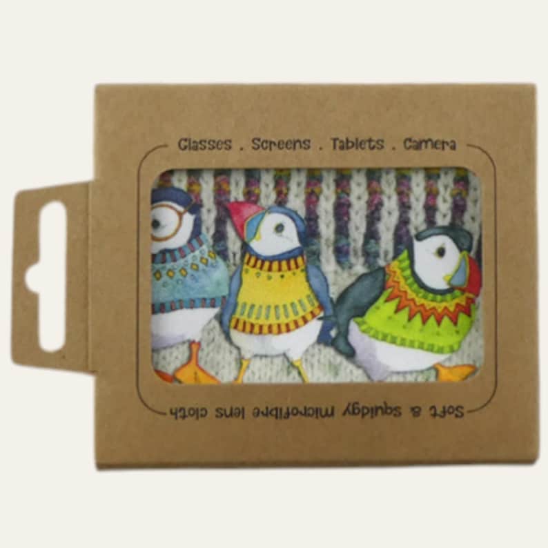 May include: A brown cardboard package with a window displaying three colorful puffin illustrations on a microfiber lens cloth. The puffins wear sweaters in blue, yellow, and green. Text on the package reads: "Glasses. Screens. Tablets. Camera."