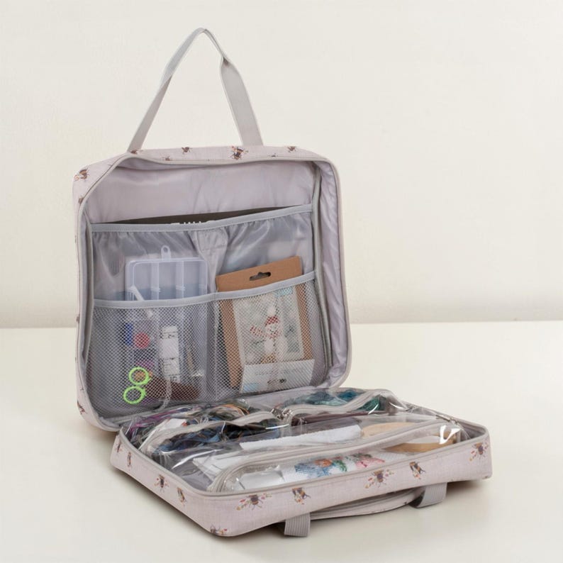 May include: Open, pale grey travel organiser with a handle and multiple compartments. The organiser is filled with various craft supplies, including small containers, spools of thread, and other sewing notions. The exterior features a subtle pattern of small brown floral designs.
