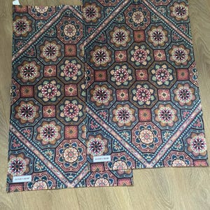 May include: Two kitchen towels featuring a geometric pattern in shades of brown, red, blue and white. The towels have a border with a floral design. The towels are labelled "Janie Crow".
